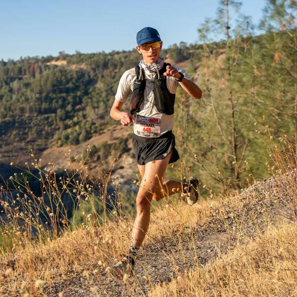 Current image: runner wearing hydration vest on trail with soft flask in front pocket